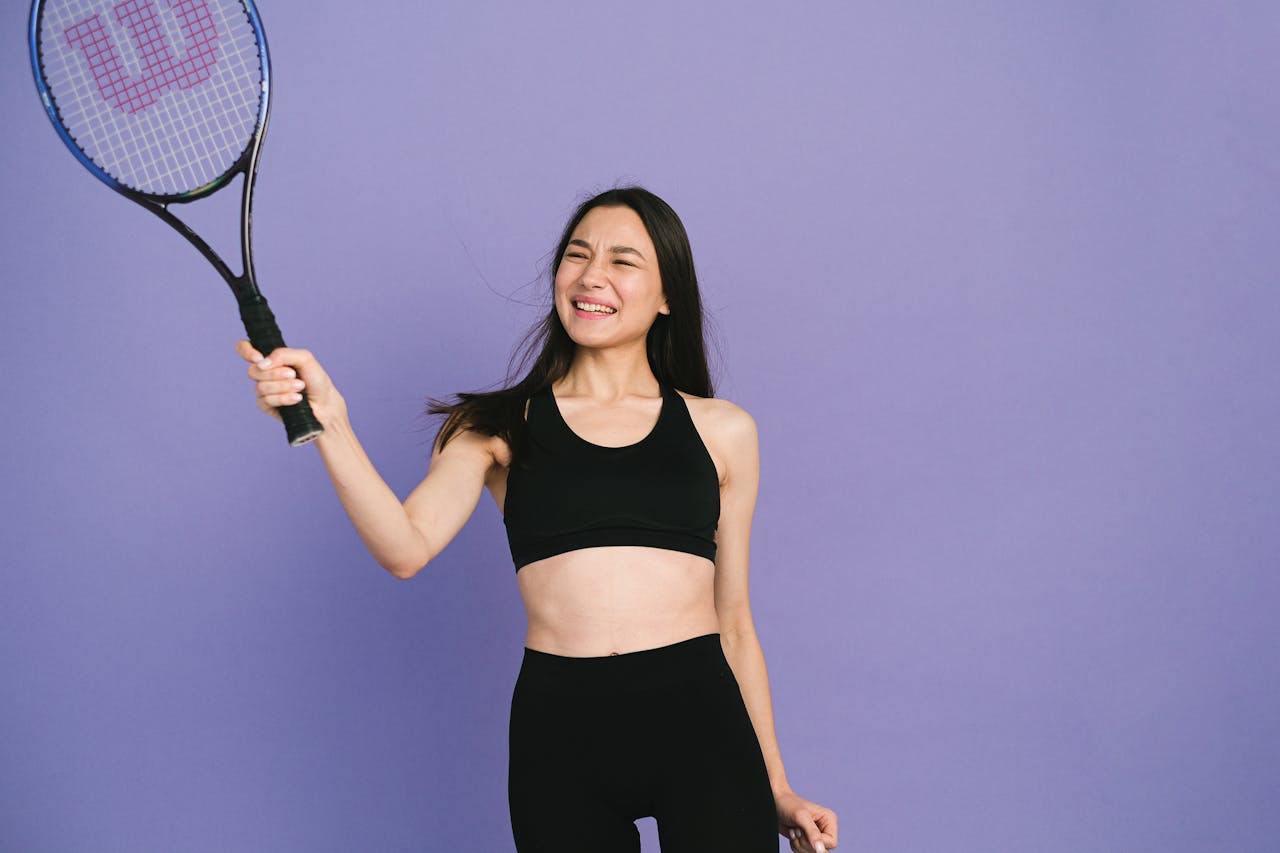Young woman in activewear holding a tennis racket, expressing joy and energy.
